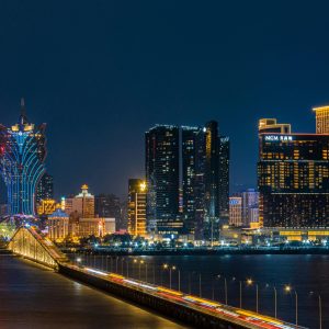 Elegant night view of Macau skyline featuring iconic illuminated hotels and a lit bridge over water.