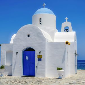 A beautiful white and blue orthodox chapel by the ocean on a sunny day.
